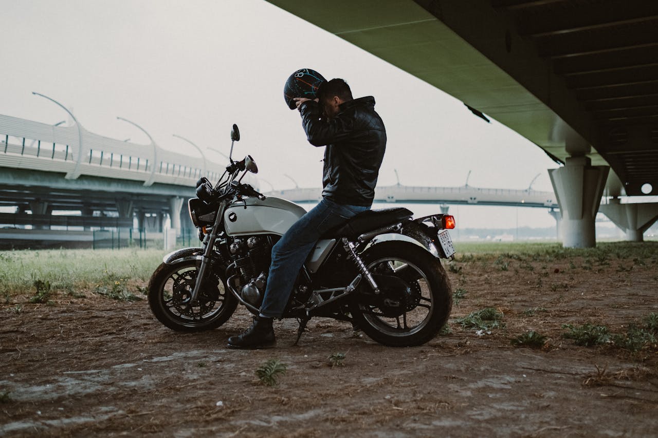 A motorcyclist putting on a helmet under a modern bridge, ready for an urban adventure.